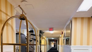 Un couloir d’hôtel avec un chariot à roulettes recouvert d’une moquette rouge, des murs à rayures et un long couloir menant à une sortie.