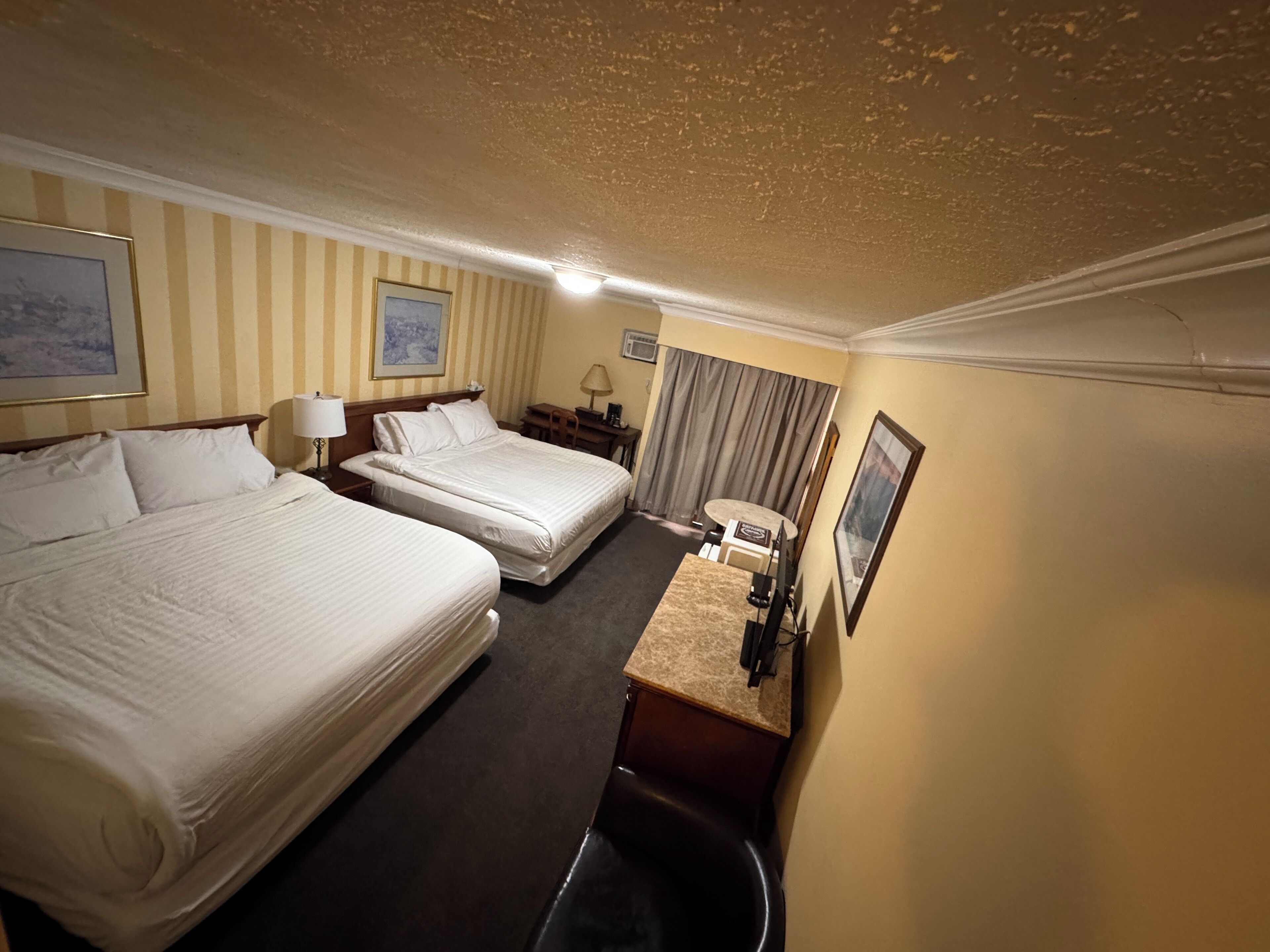 Ein Hotelzimmer mit zwei Betten, einem Schreibtisch, einem Stuhl, einer Lampe und einem kleinen Tisch.