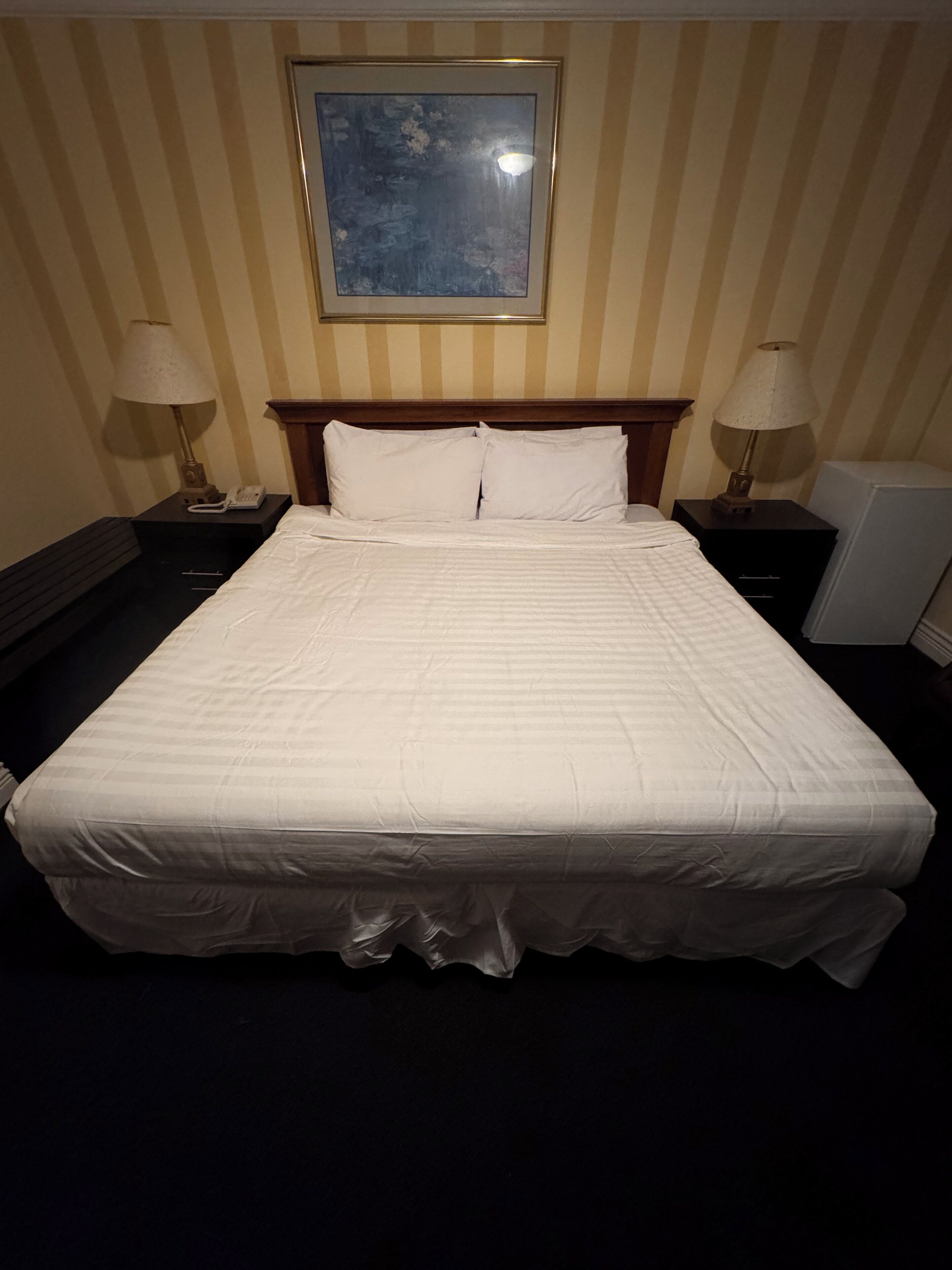 A hotel room with a large bed, two bedside tables, a nightstand, a lamp, and a framed picture on the wall.