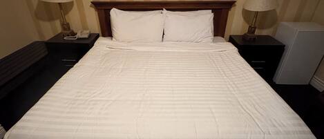 A hotel room with a large bed, two bedside tables, a nightstand, a lamp, and a framed picture on the wall.