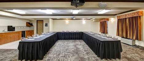 A conference room with a long table, chairs, a projector, and a kitchenette.