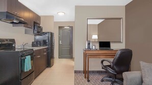 A compact kitchen with modern appliances, a dining area with a table and chair, and a small seating area with a couch. - Super 8 by Wyndham Athabasca AB (Athabasca)
