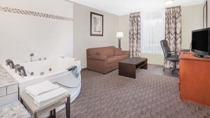 A hotel room with a large bathtub, a brown sofa, a desk with a television, and a chair. - Super 8 by Wyndham Athabasca AB (Athabasca)