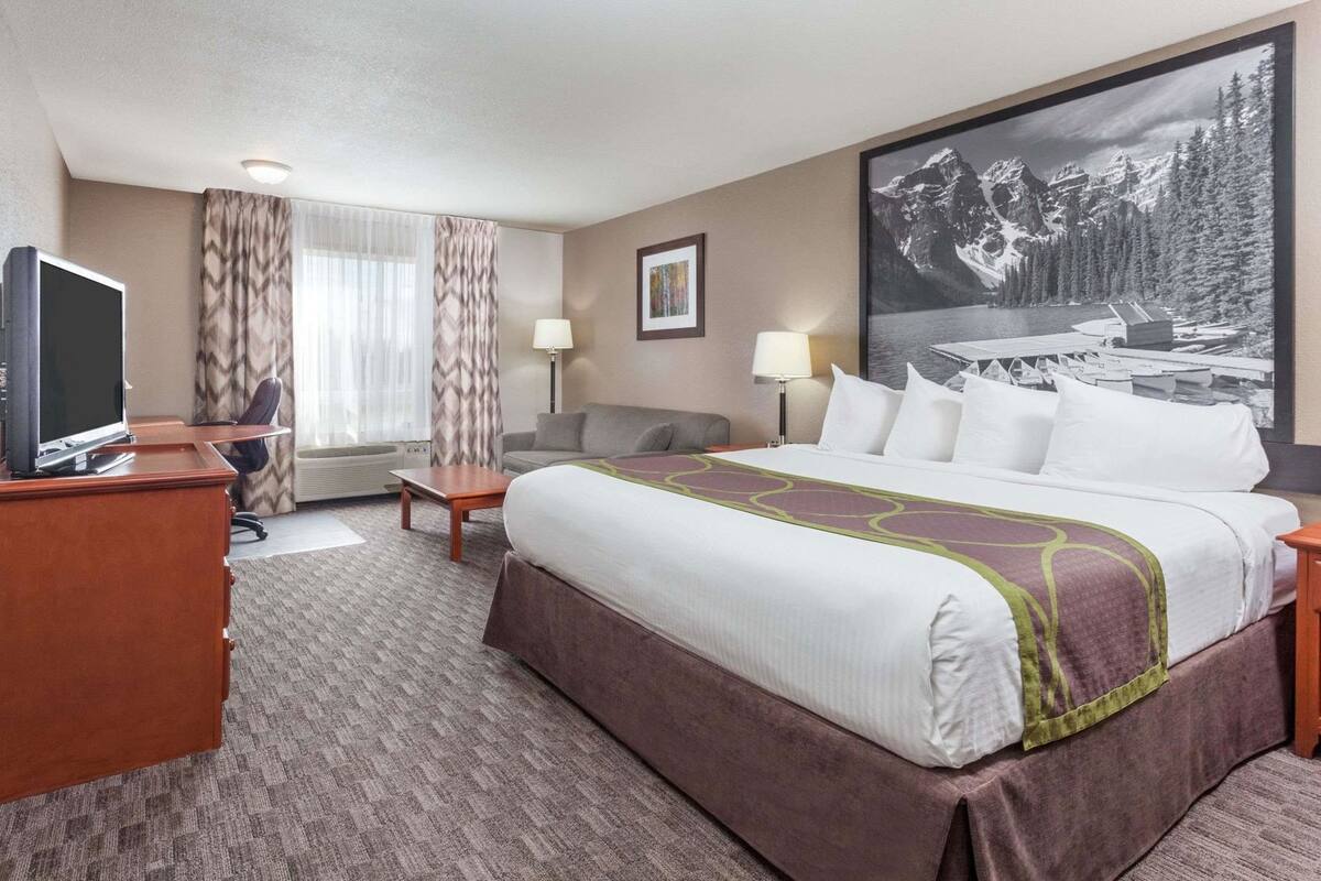 A hotel room with a bed, a desk, a chair, a television, a window with curtains, and a large framed picture on the wall.
