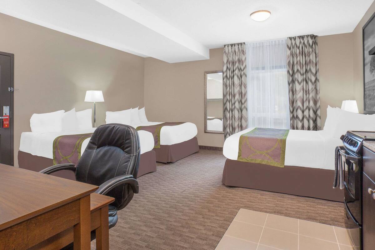 A hotel room with two beds, a desk, a chair, a coffee maker, and a large window with curtains.