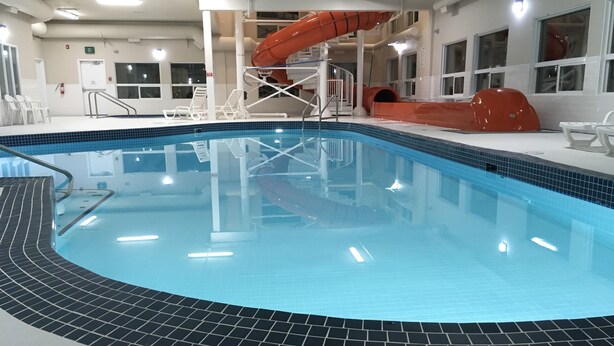 An indoor swimming pool with a slide, tiled flooring, and a clear blue water surface. - Super 8 by Wyndham Athabasca AB (Athabasca)