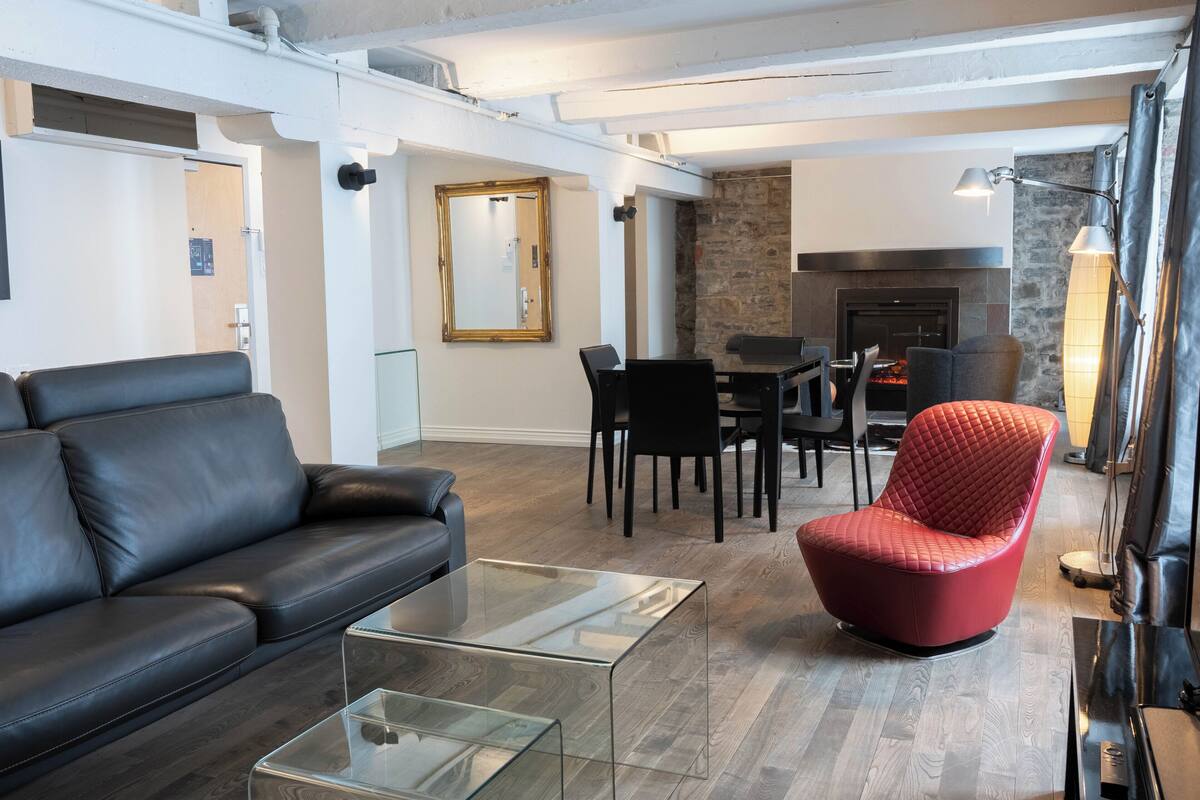 A modern living room with a leather sofa, a glass coffee table, a red chair, a fireplace, and a dining area.