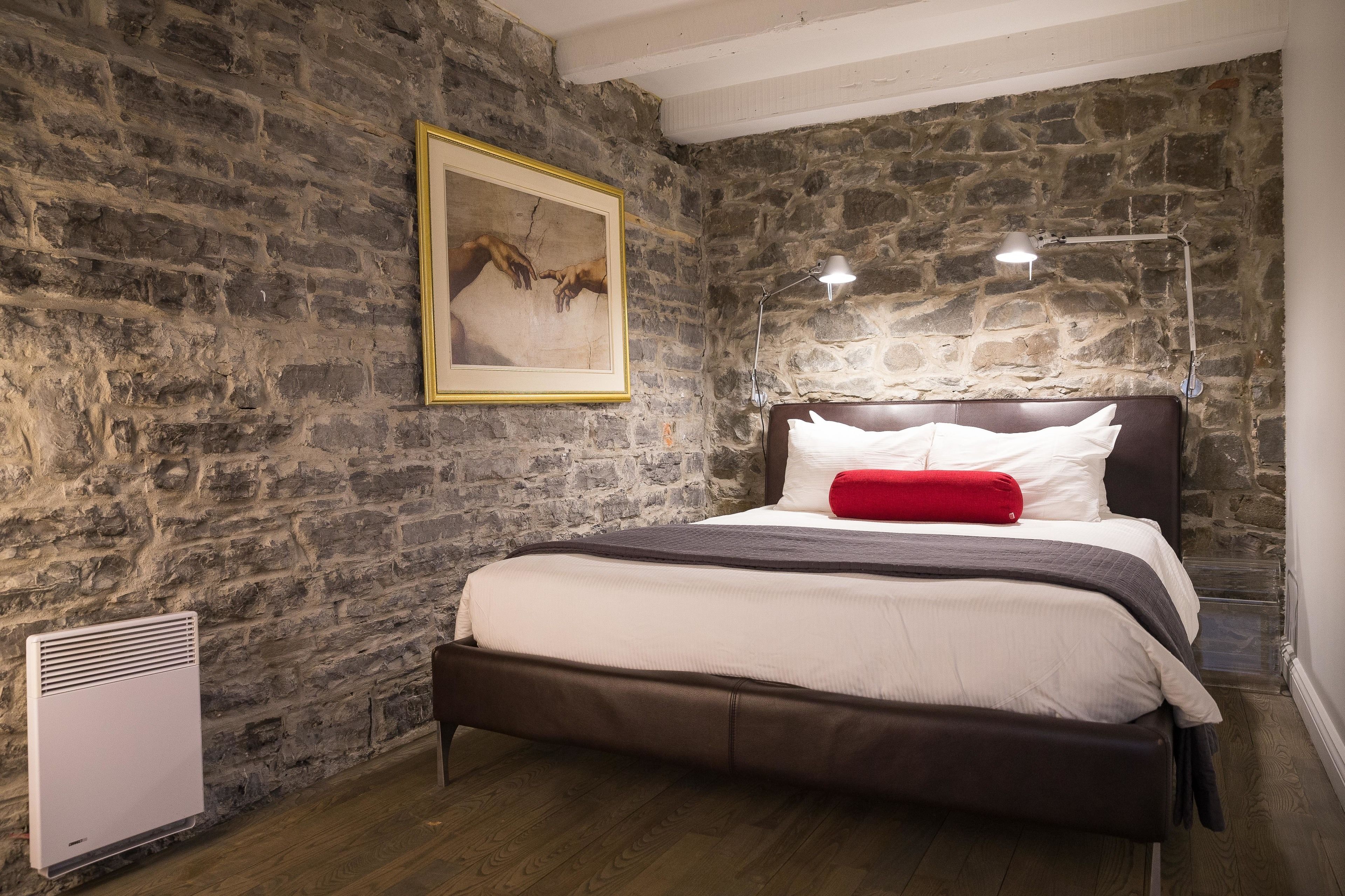 Ein Schlafzimmer mit Steinsandsteinwand, einem Bett mit weißer und roter Bettwäsche sowie einem gerahmten Bild an der Wand.
