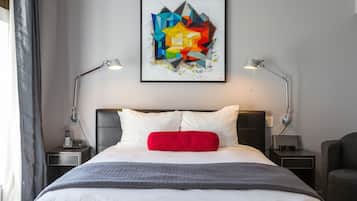 Una cama bien hecha con almohadas blancas y rojas, una manta gris y dos lámparas de noche.