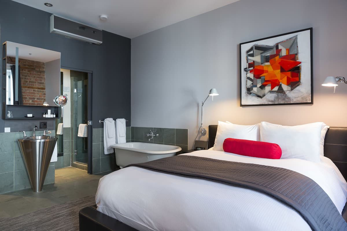 A modern hotel room with a large bed, a bathroom with a bathtub, and a large abstract painting on the wall.