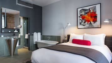 A modern hotel room with a large bed, a bathroom with a bathtub, and a large abstract painting on the wall.