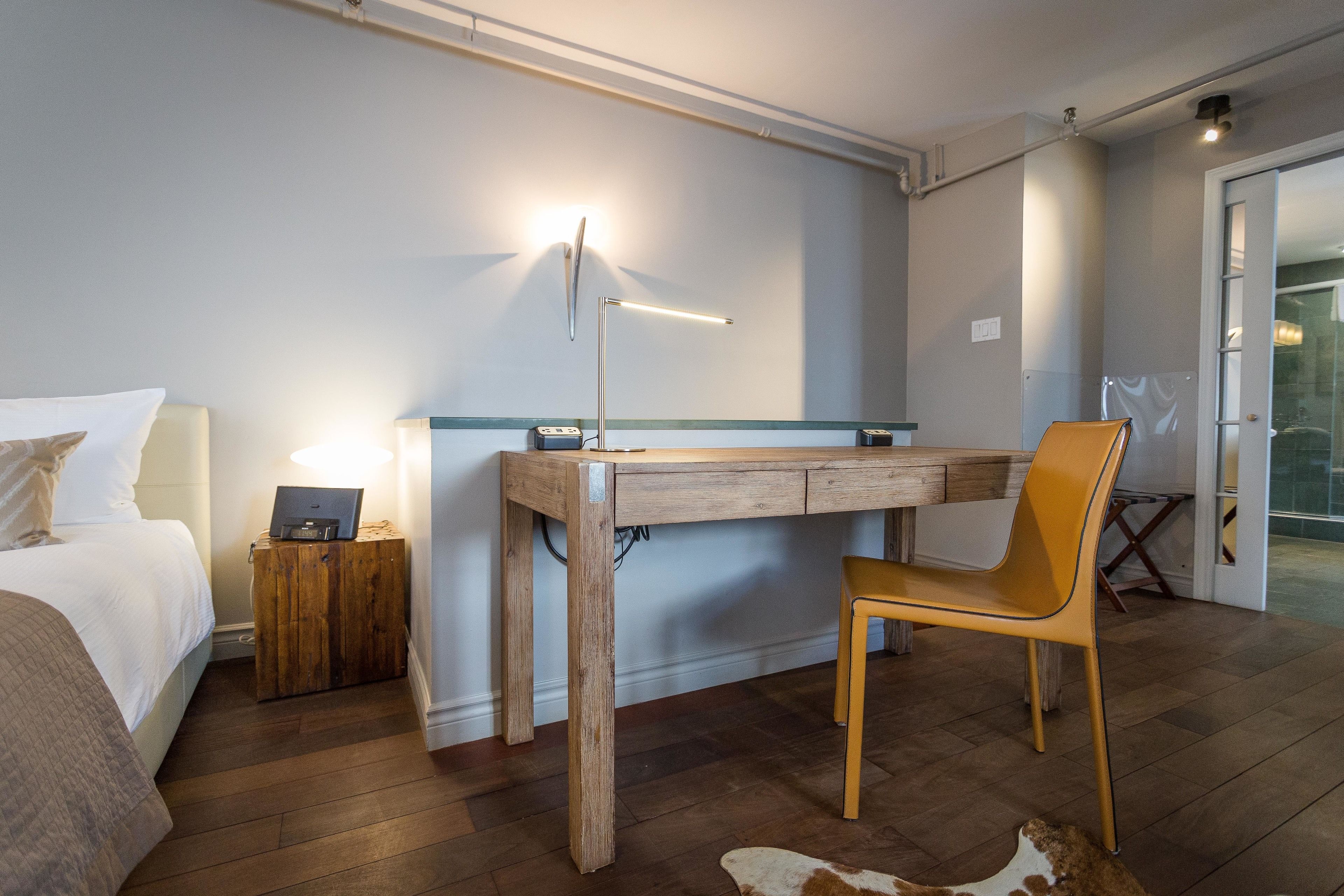 Ein Hotelzimmer mit Bett, Schreibtisch, Stuhl, Lampe und einem kleinen Schrank.