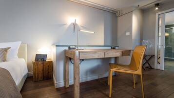 A hotel room with a bed, a desk, a chair, a lamp, and a small cabinet.