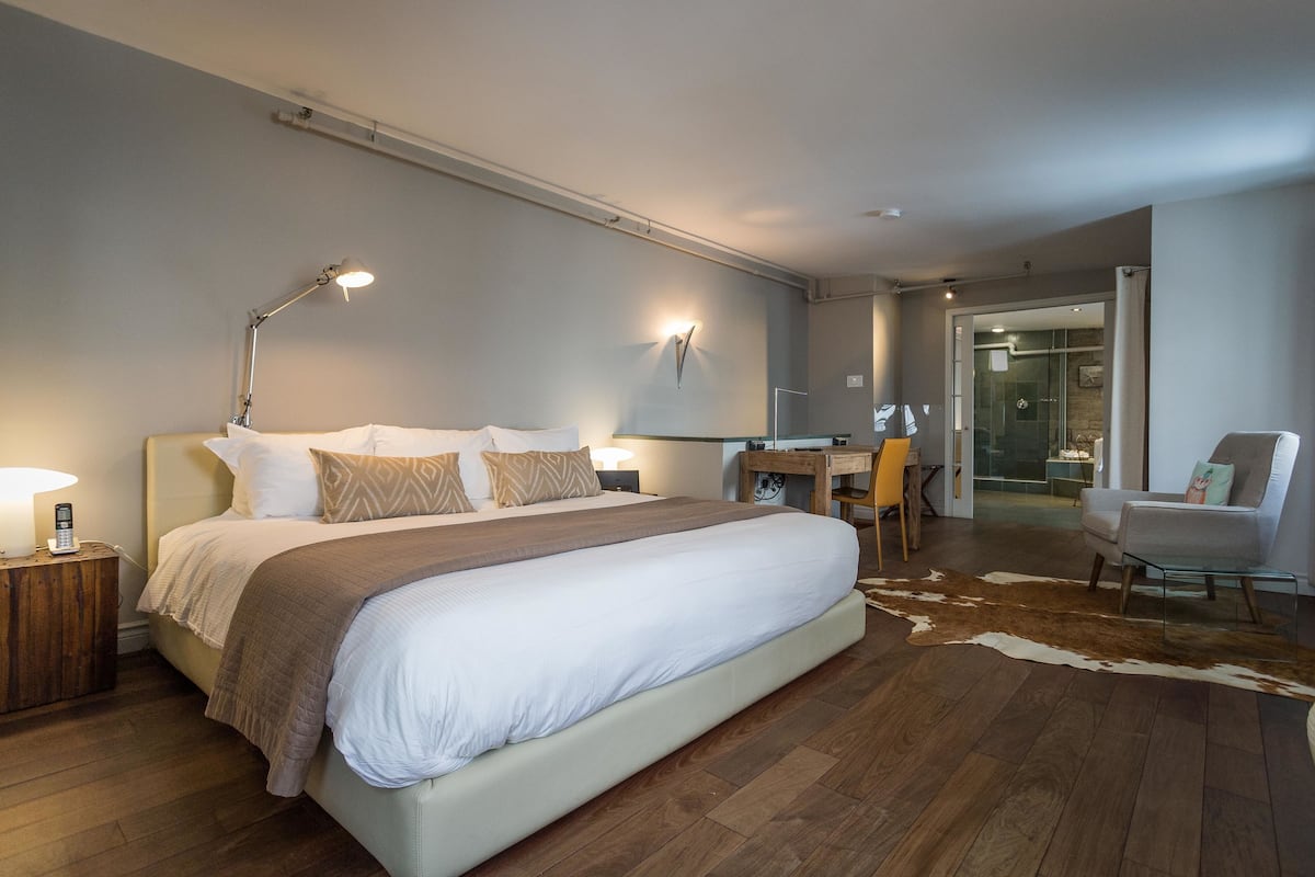 A modern hotel room with a large bed, a desk, a chair, and a glass shower area.