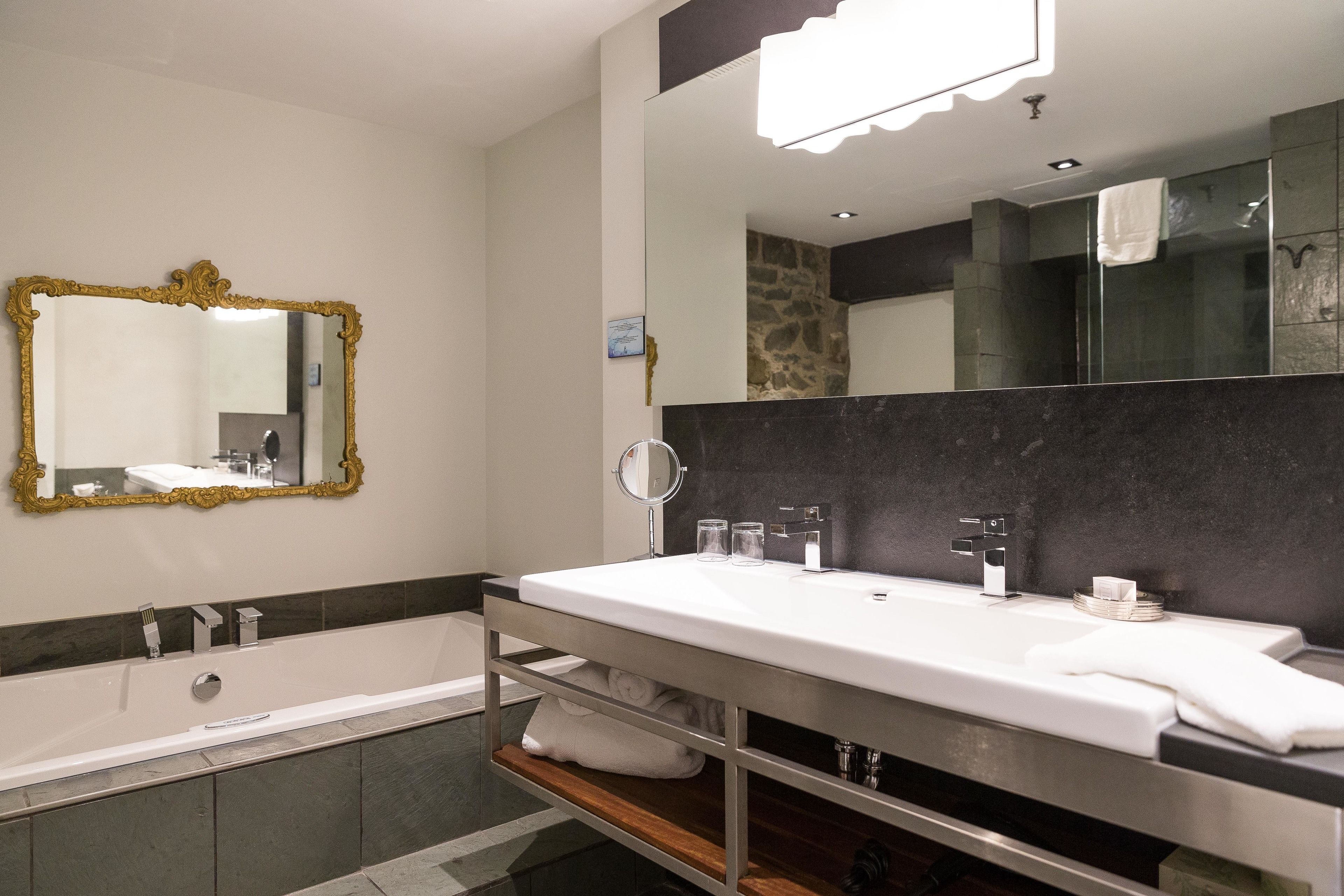 A modern bathroom with a large white sink, a gold-framed mirror, and a bathtub.
