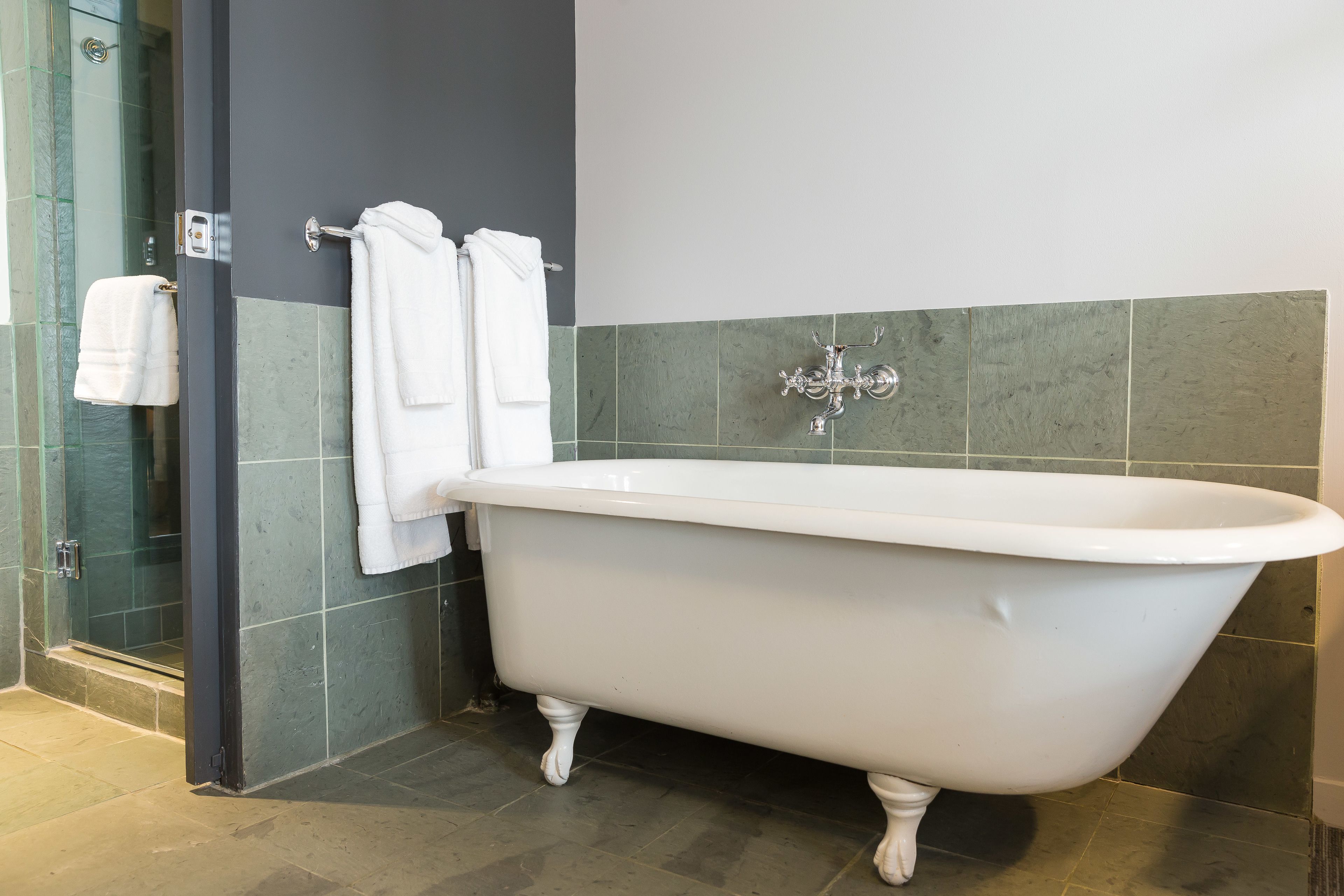 Un baño con una bañera independiente, una cabina de ducha de vidrio y dos toallas colgadas en un perchero.