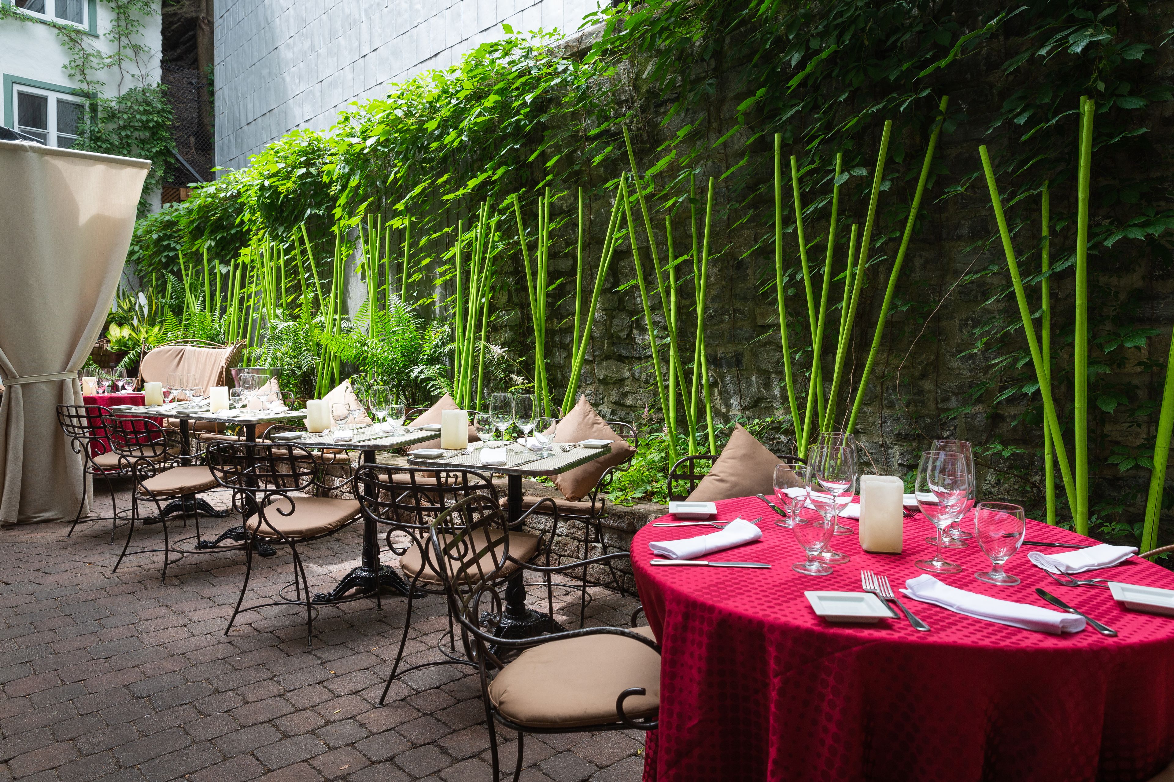 An outdoor dining area with tables set for two, surrounded by lush greenery and bamboo plants.
