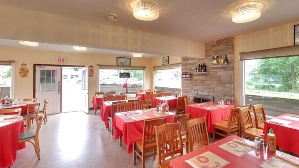 Un restaurante con varias mesas cubiertas con manteles rojos, sillas de madera y una chimenea de piedra.