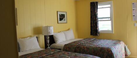 A room with two beds, a window with curtains, a lamp, and a framed picture on the wall.