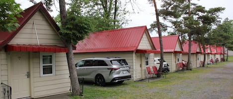 A row of cabins with red roofs and beige walls, each with a door and window, and a gravel path in front.