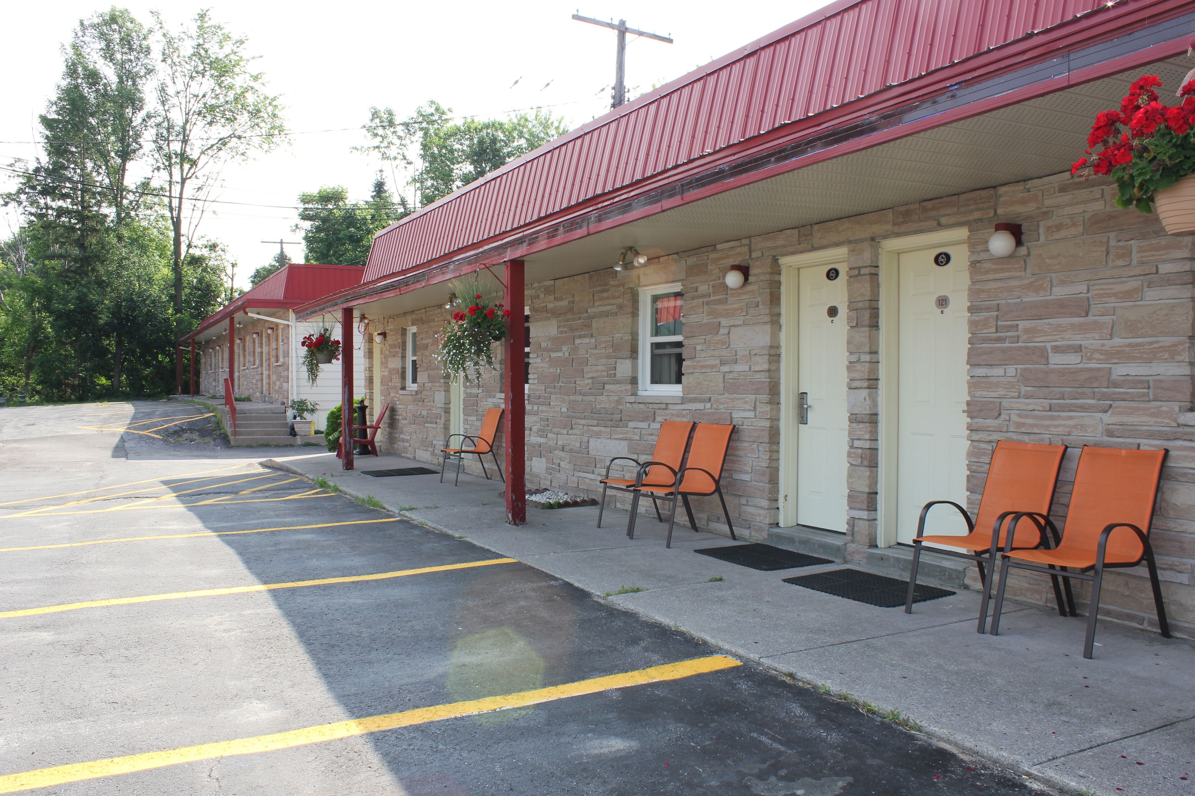 A motel with a red roof, stone facade, and outdoor seating area with orange chairs.