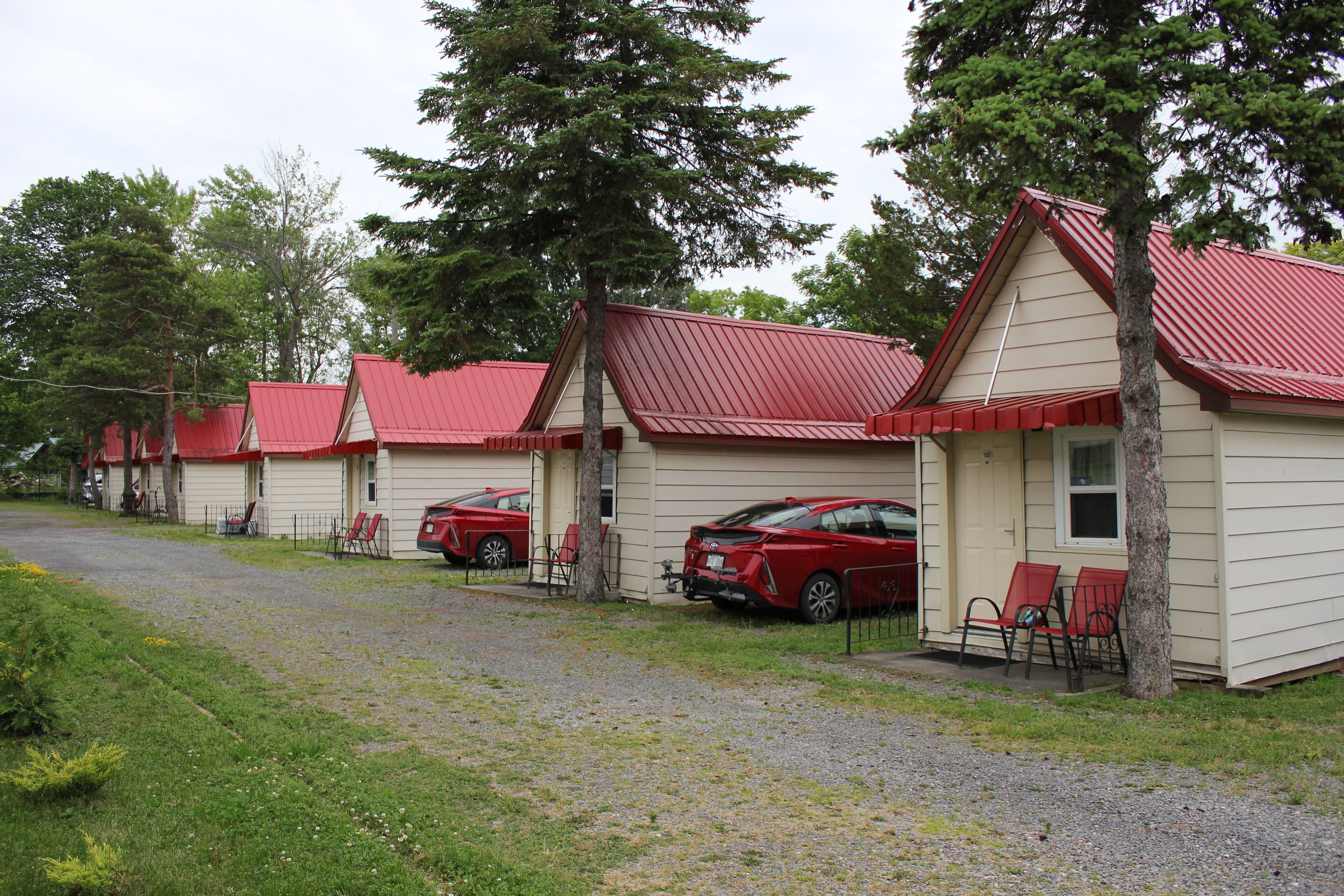 A row of small, single-story cabins with red roofs, each featuring a front porch and a car parked outside.