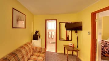 Ein Hotelzimmer mit einem karoüberzogenen Sofa, einem kleinen Tisch, einem Fernseher und einem Bett mit floralem Bettbezug.