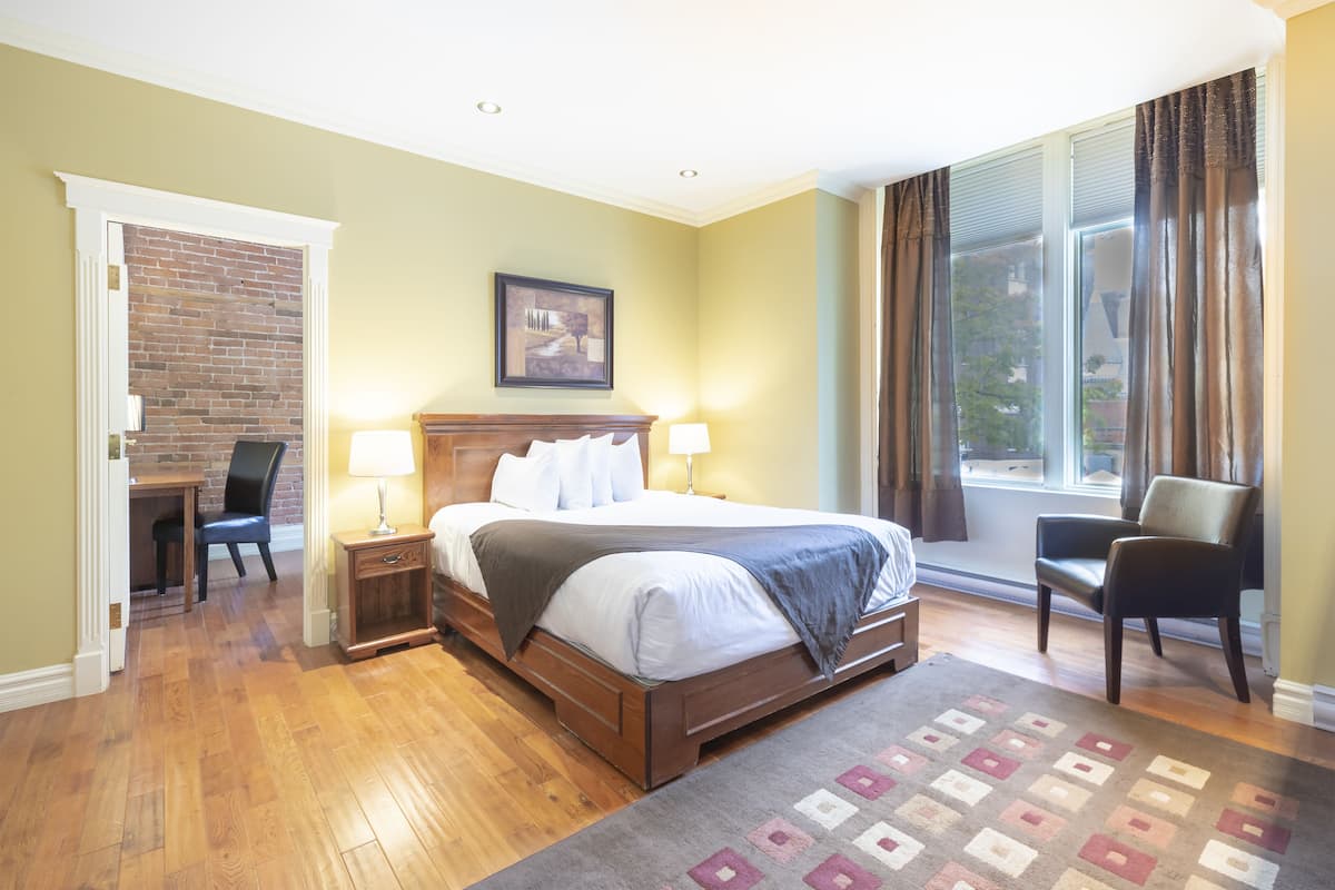 Un dormitorio con una cama de madera, dos mesitas de noche con lámparas, una silla, un tapete y una pared de ladrillo.