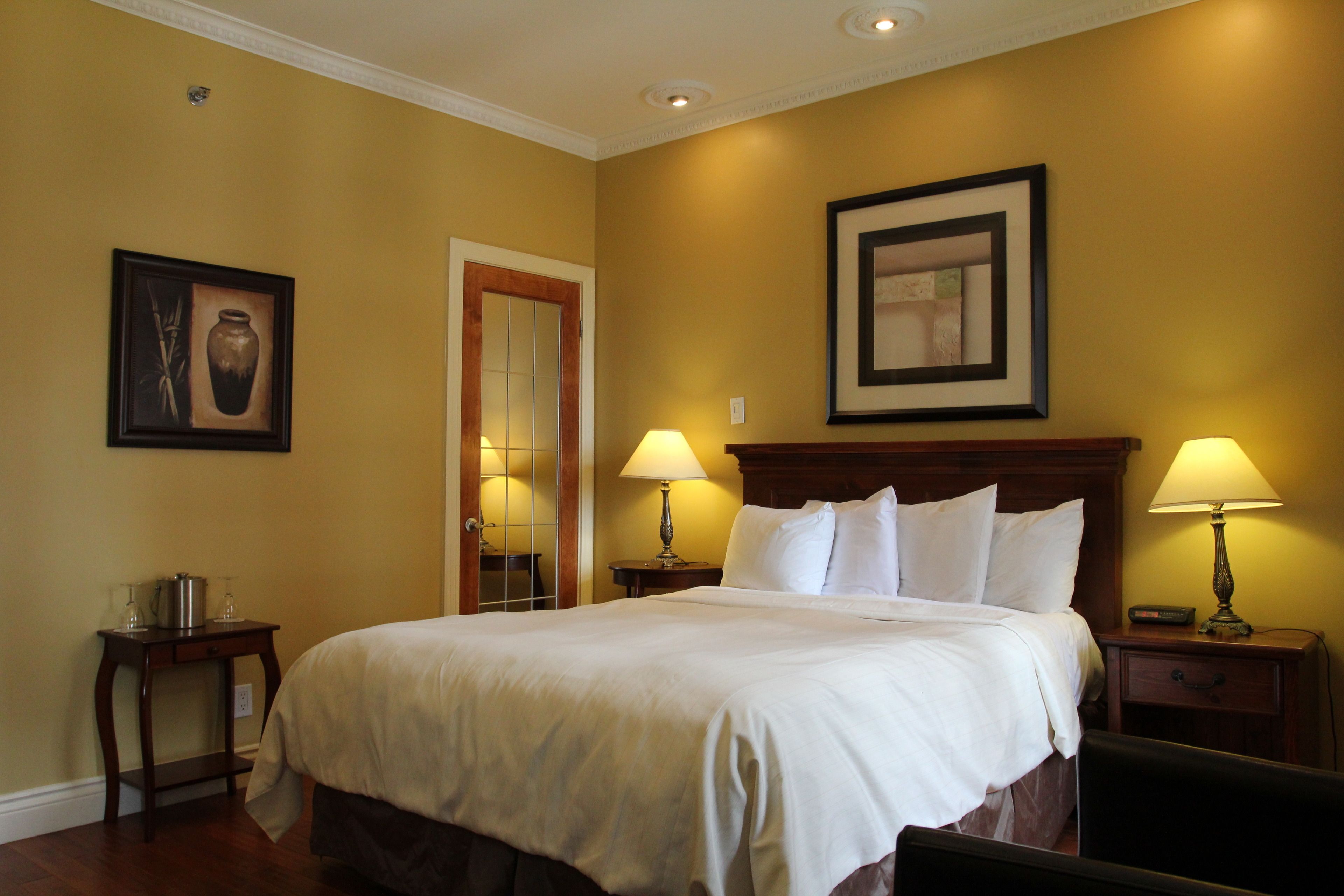 A hotel room with a large bed, two bedside tables with lamps, a wooden headboard, and framed artwork on the walls.