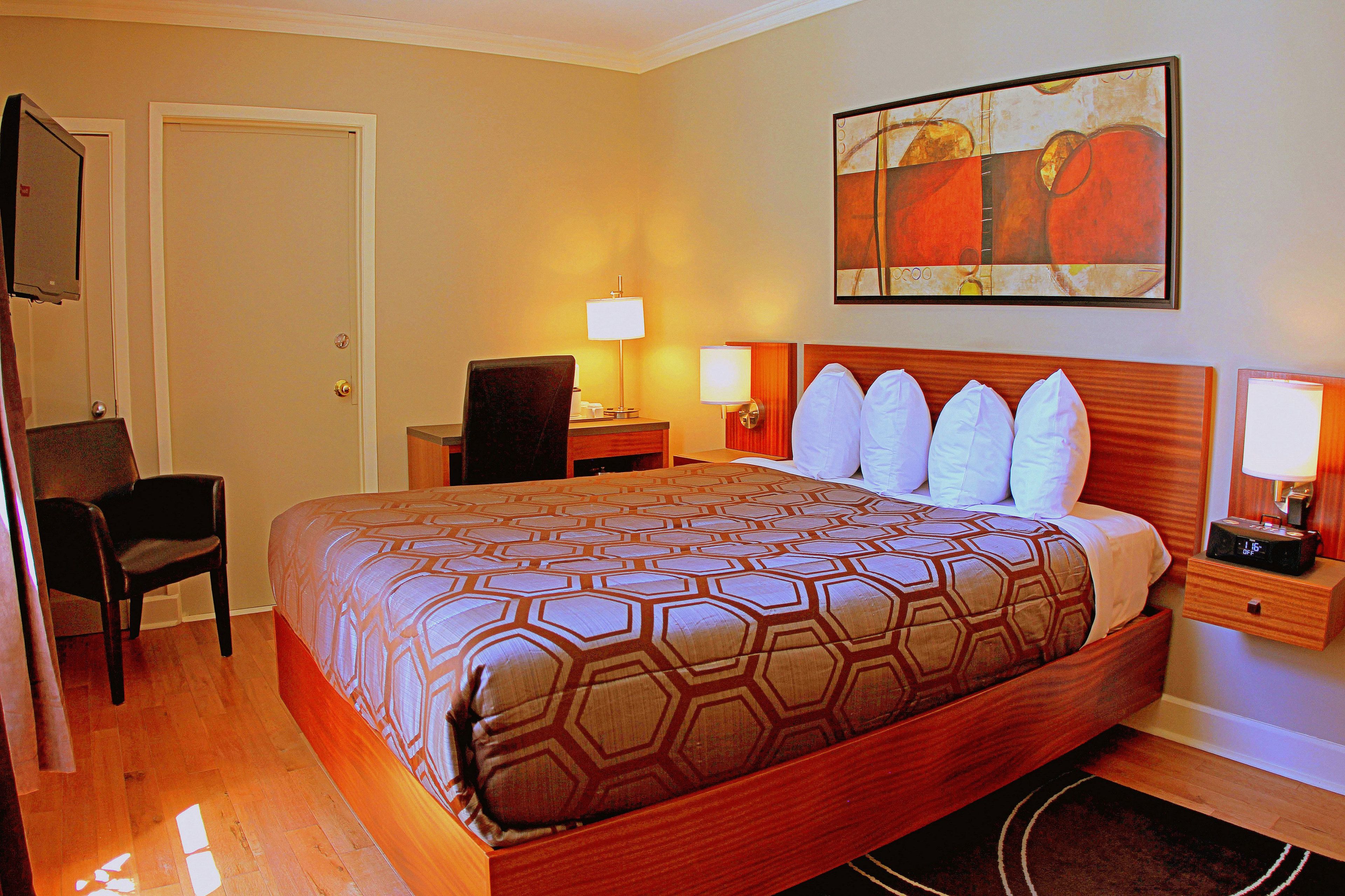 A hotel room with a large bed, a desk with a chair, a TV, and a painting on the wall.