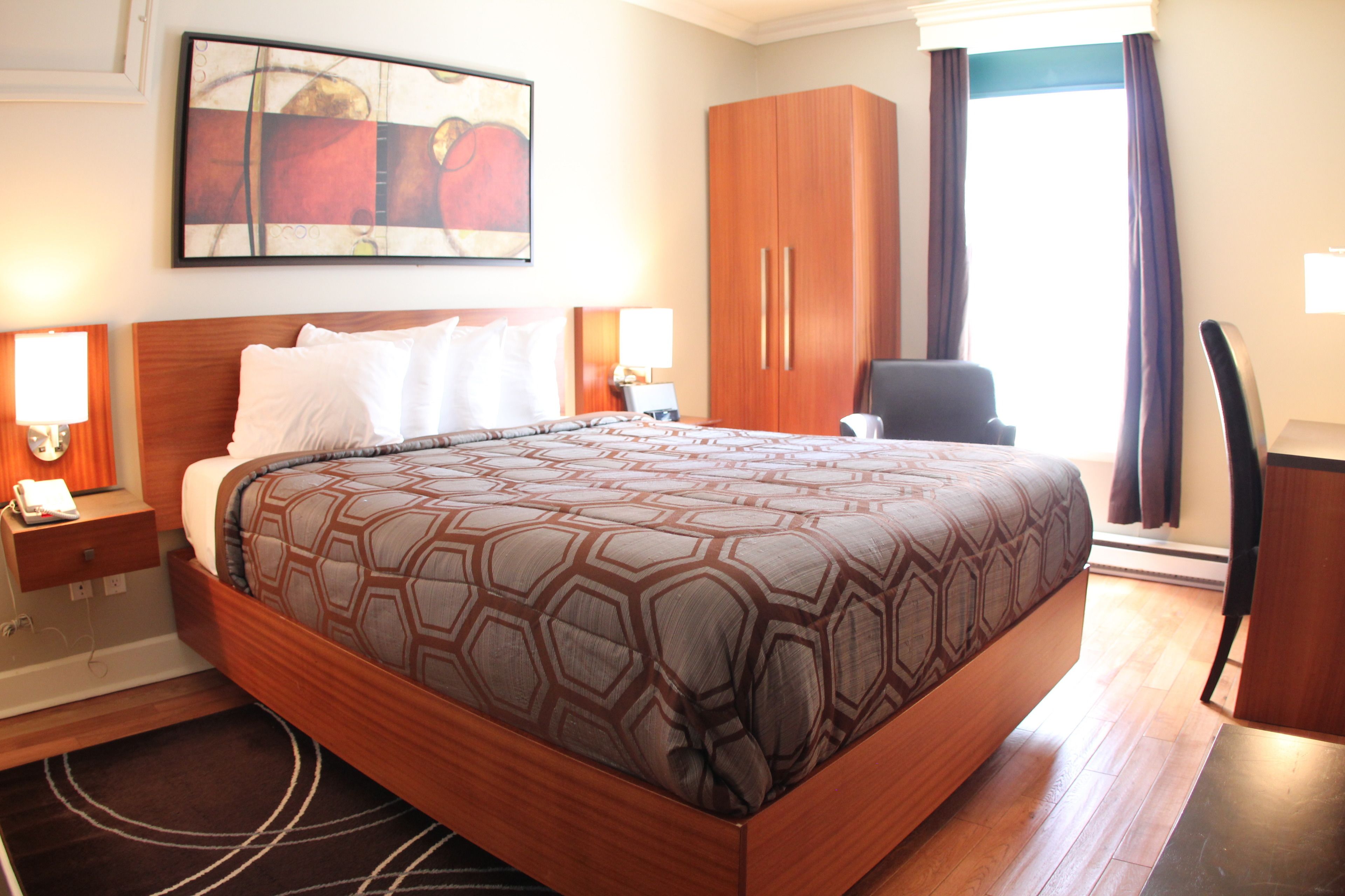 A hotel room with a large bed, wooden wardrobe, and a painting on the wall.