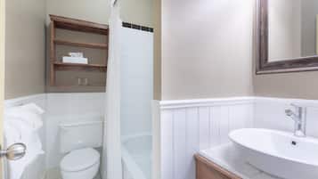 A bathroom with a white toilet, a bathtub, a wooden shelf with a tissue box, and a large mirror.