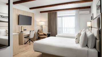 A hotel room with a large bed, a desk, a chair, a TV, and a window with curtains.
