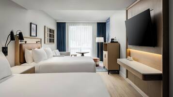 Habitación de hotel con dos camas, televisión, escritorio y ventana con cortinas.