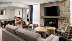 A modern living room with a stone fireplace, a flat-screen TV, a sofa, a dining table, and a coffee table. - Mont Gabriel, Sainte-Adele, a Tribute Portfolio Resort (Sainte-Adele)