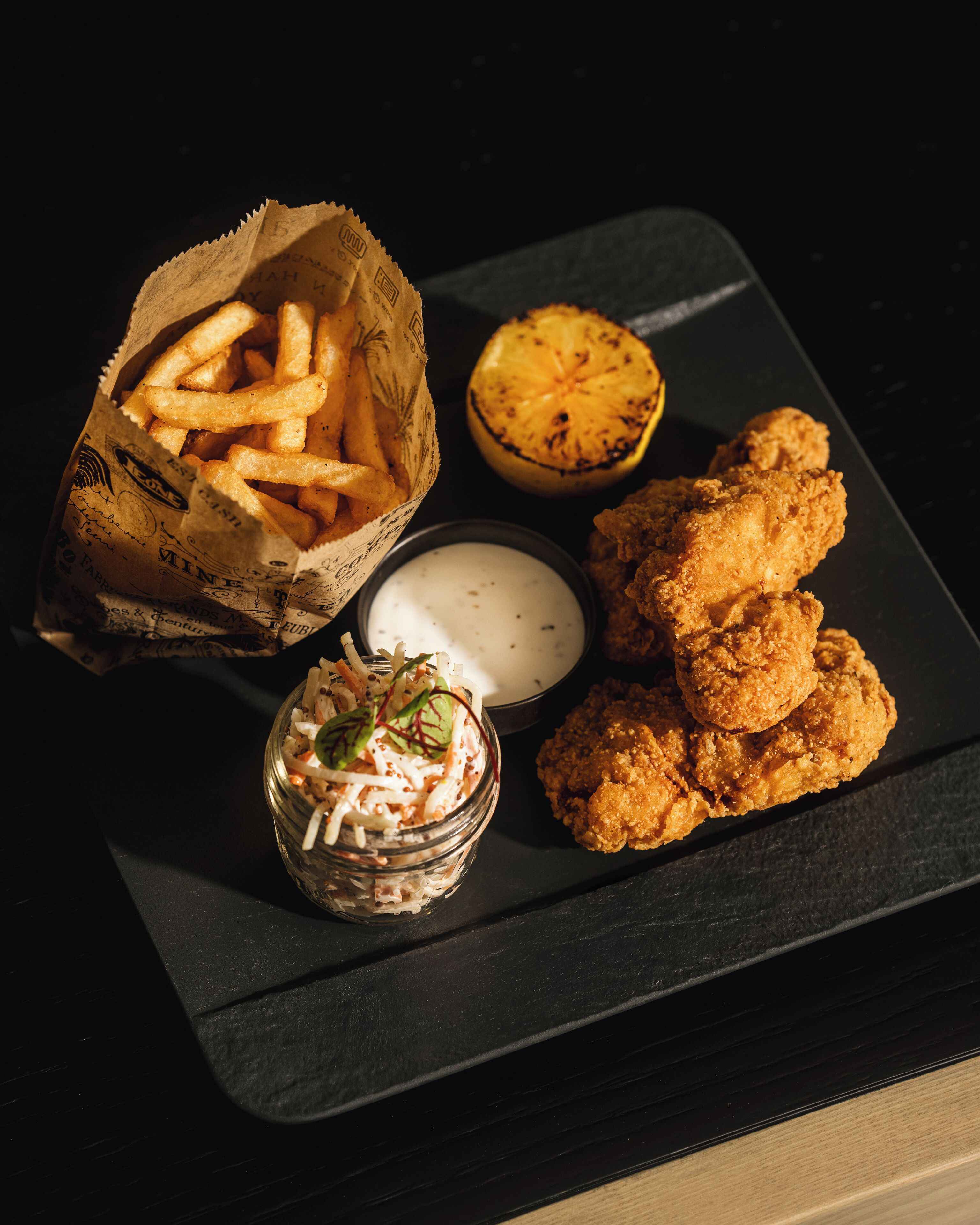 Une assiette contenant du poulet frit, des frites, un demi-citron grillé et une petite portion de salade de chou.