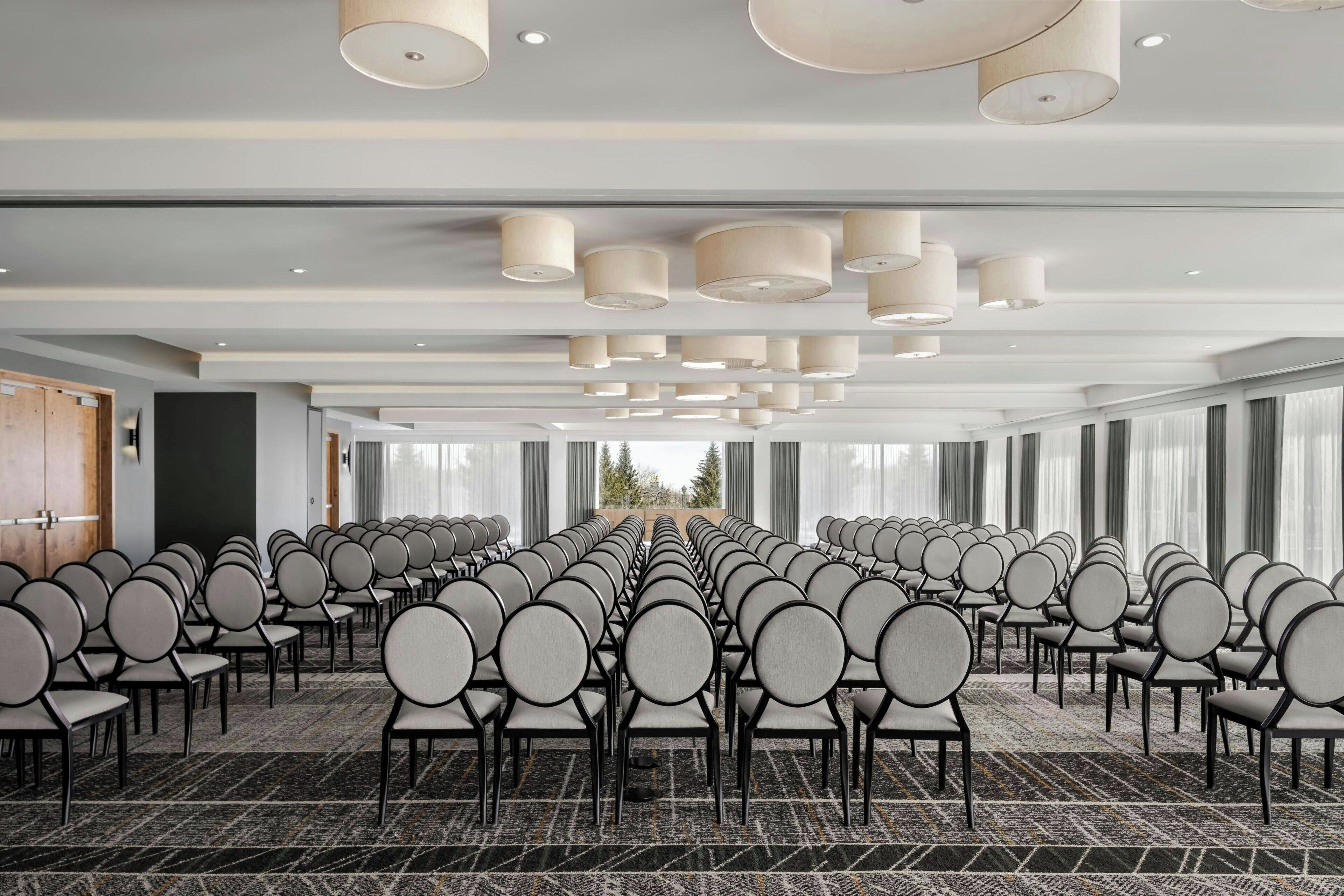Ein Konferenzraum mit Reihen von Stühlen, großen Fenstern und modernen Deckenleuchten.