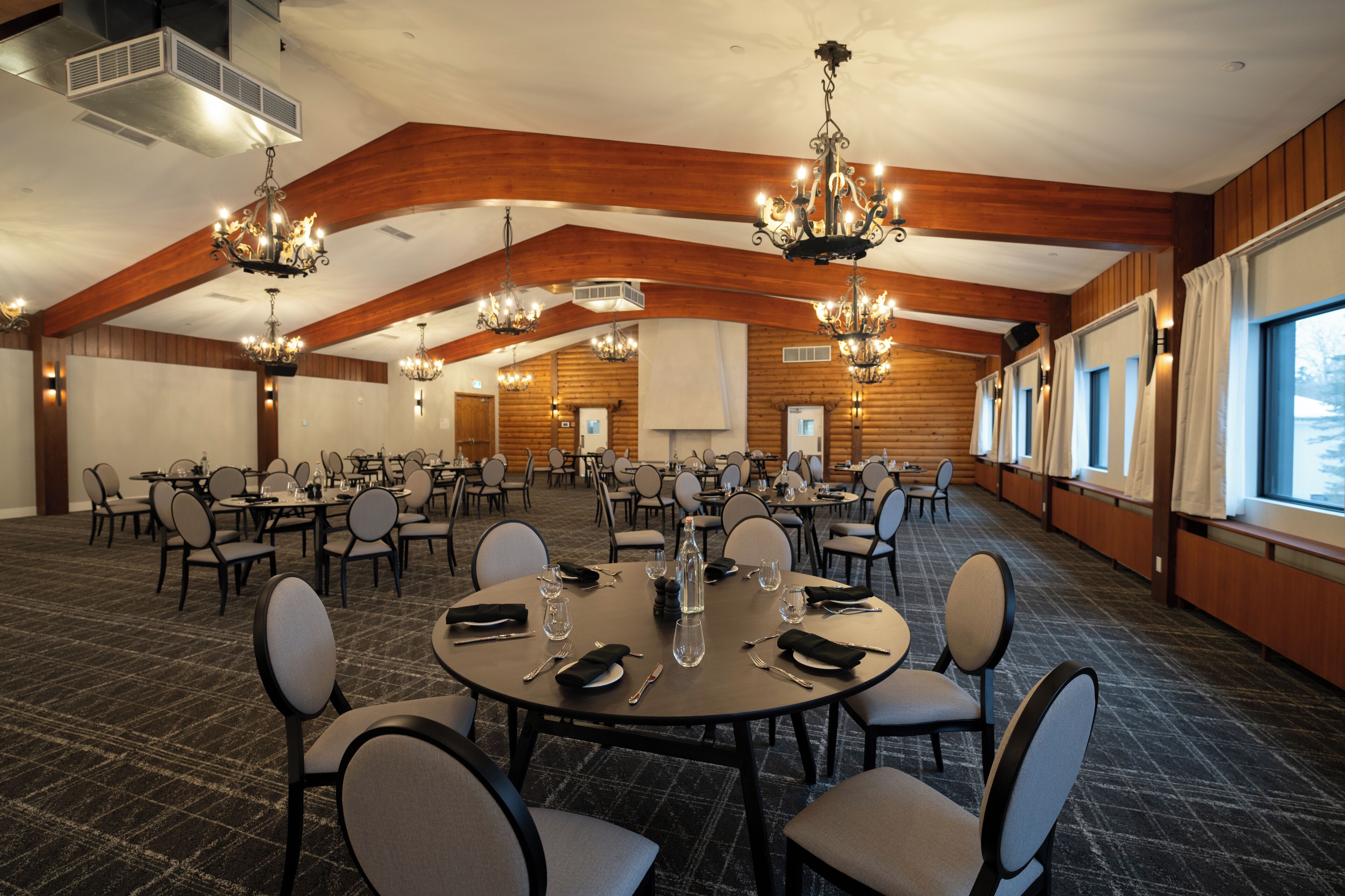 A conference room with multiple tables and chairs, wooden paneling, and chandeliers.