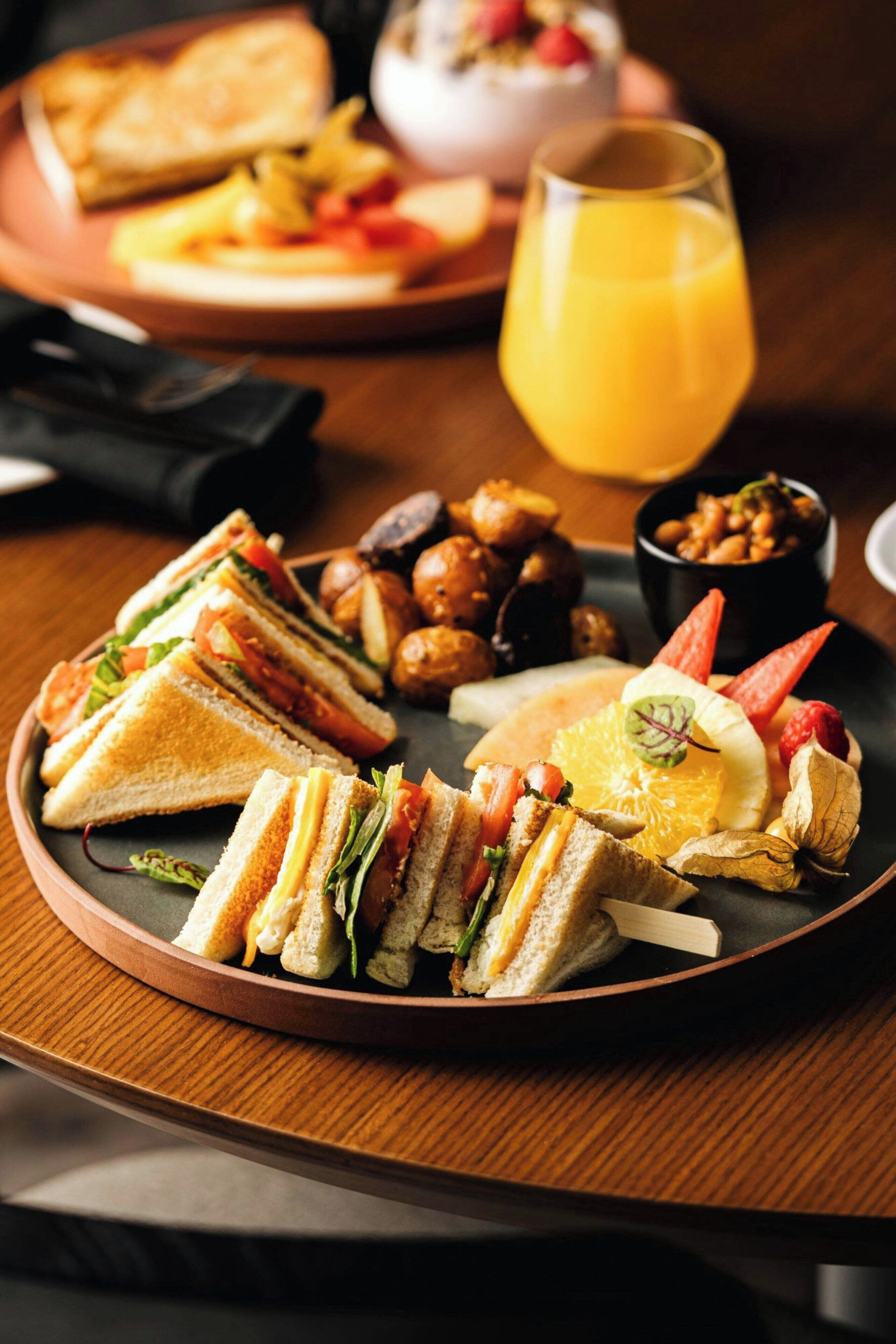 Une assiette de petit-déjeuner avec des sandwichs, des fruits et un verre de jus d’orange.