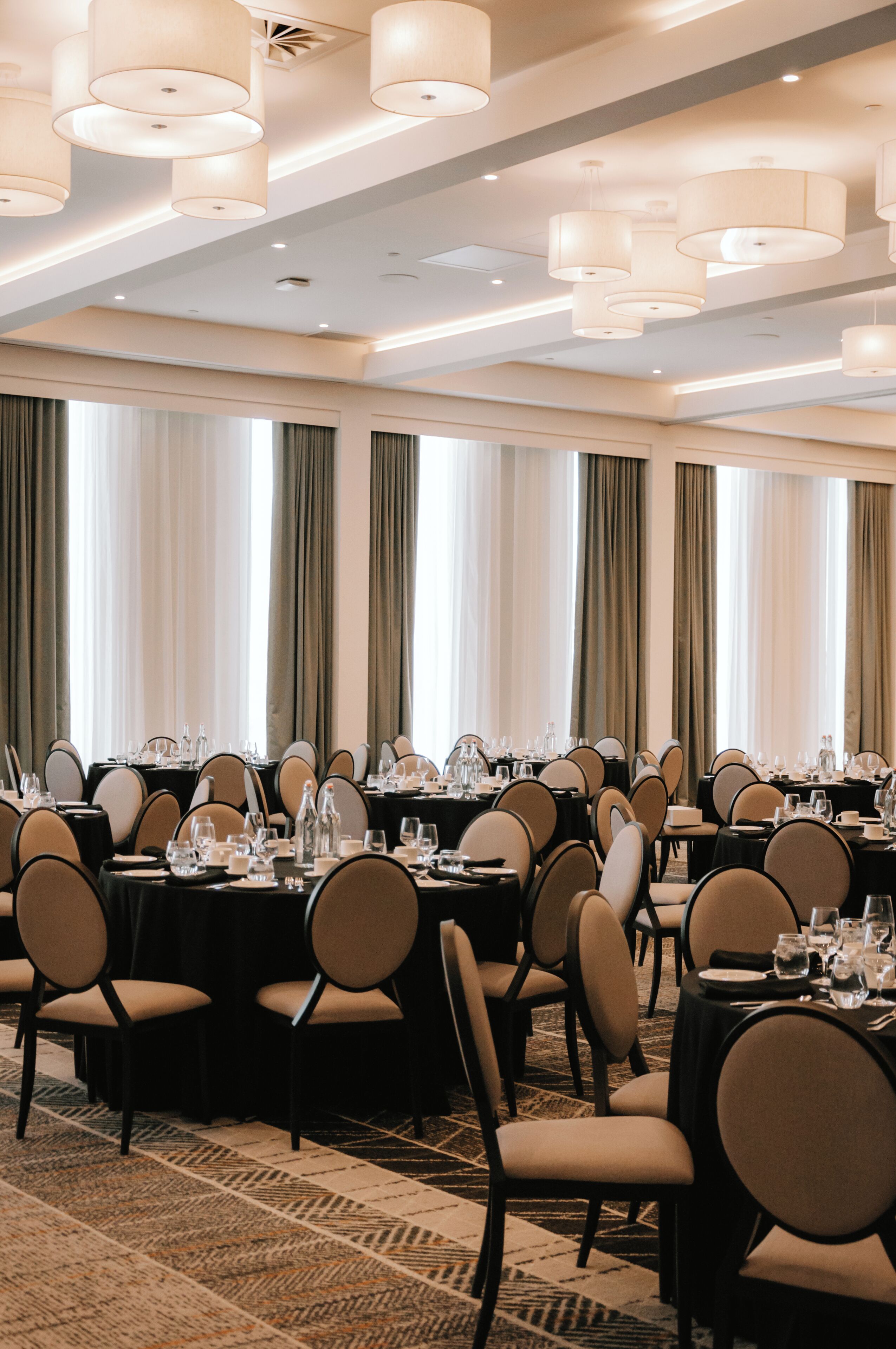 Une salle de banquet avec des tables rondes, des chaises et un tapis à motifs.