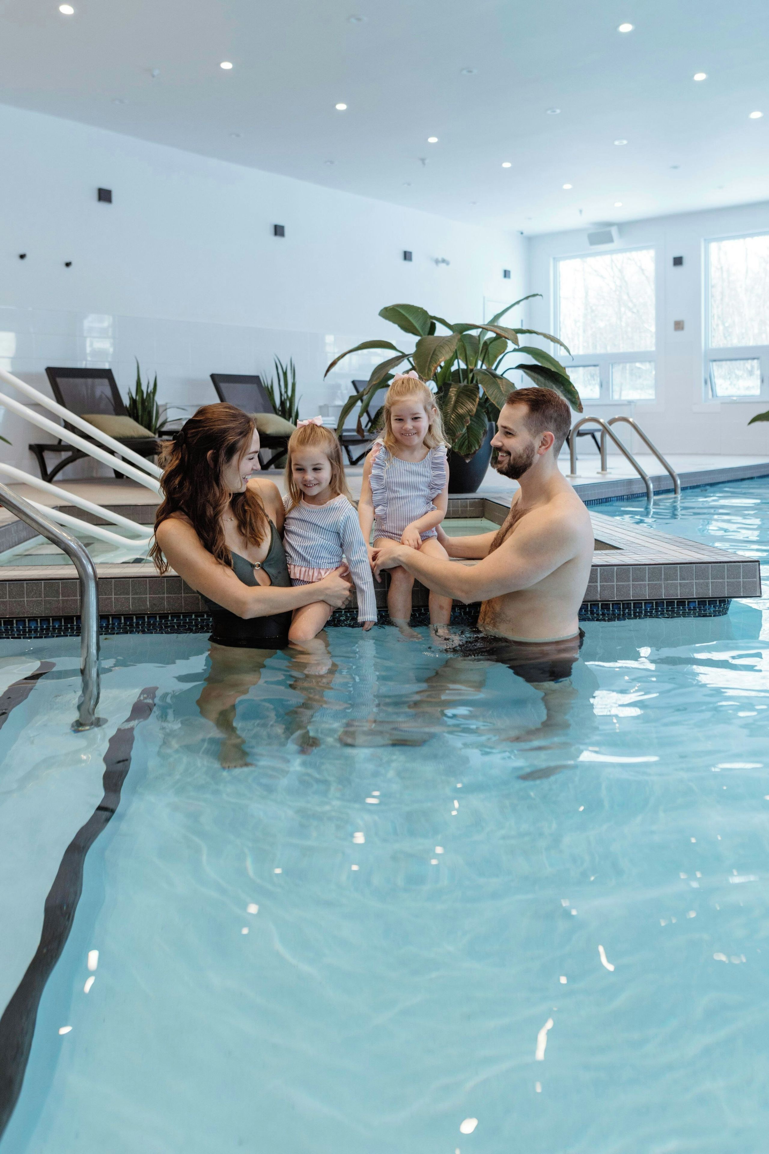 Una familia de cuatro personas en una piscina con un ambiente interior moderno, que incluye una escalera y plantas en macetas.