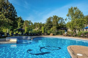 Une piscine d’eau cristalline, entourée de chaises longues et de parasols, avec des arbres en arrière-plan.