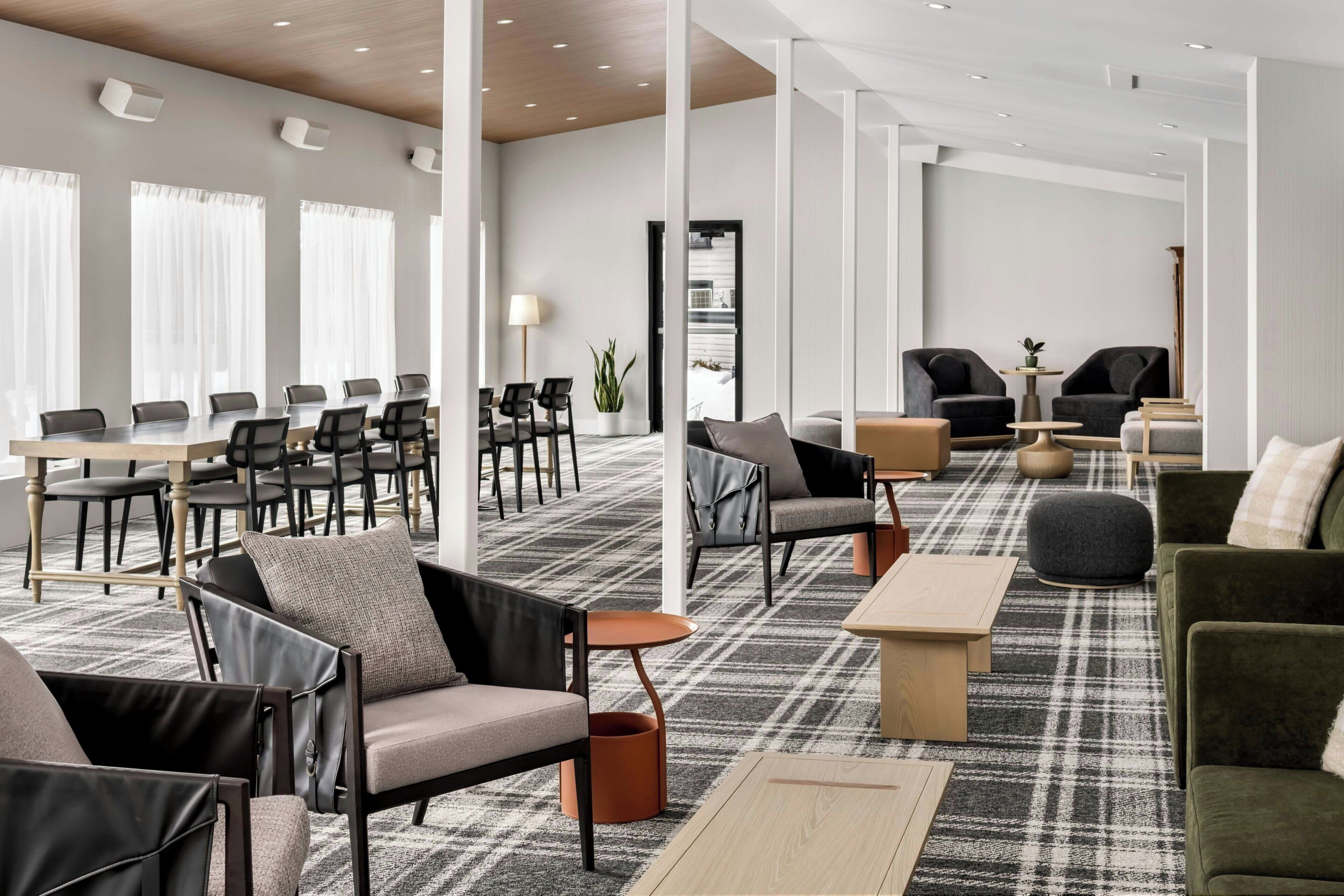 Een moderne hotellobby met een grote vergadertafel, meerdere banken en een kamerbreed tapijt.