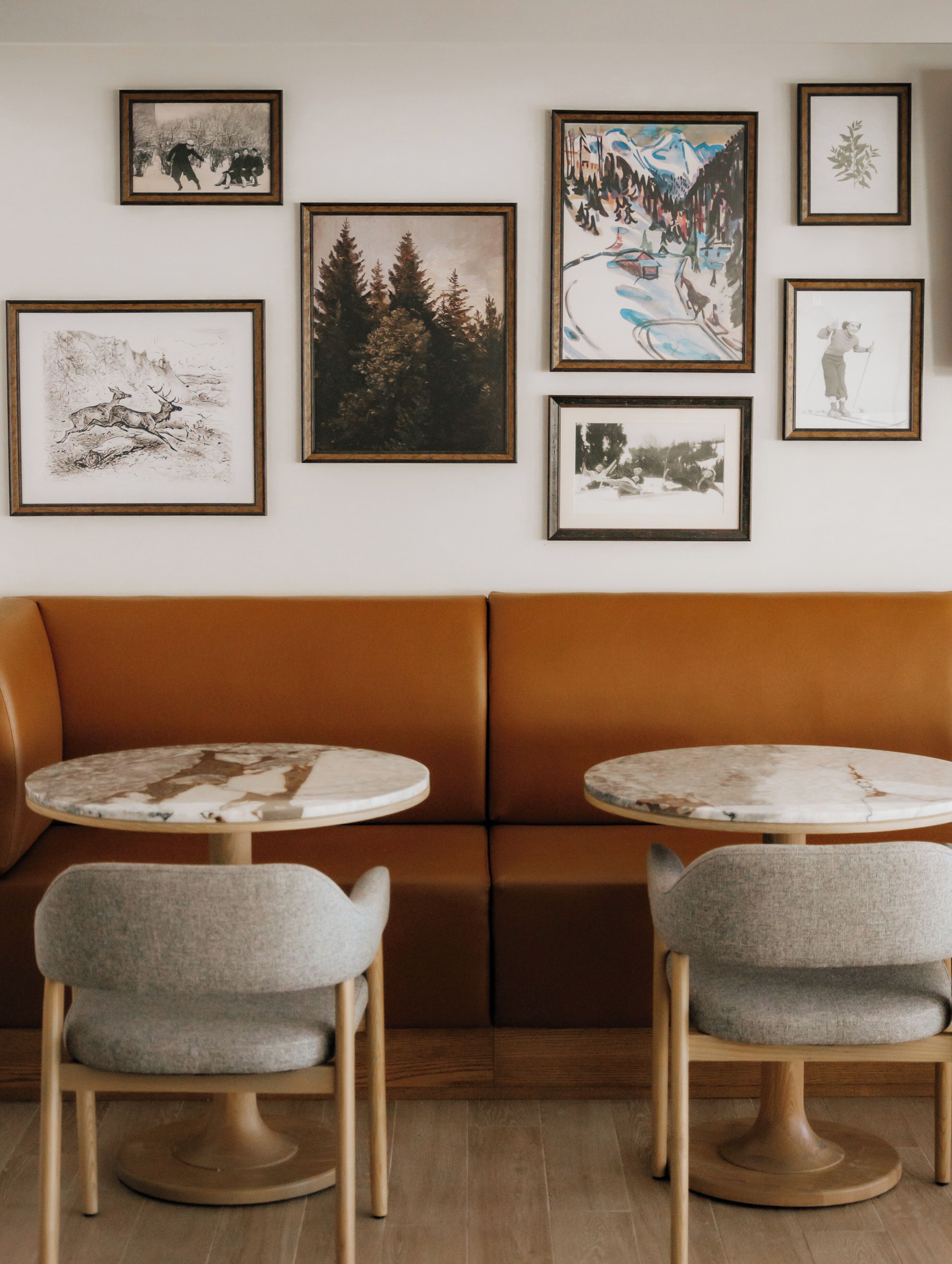 Une pièce avec un canapé marron, deux tables rondes avec des chaises et six tableaux encadrés accrochés au mur.
