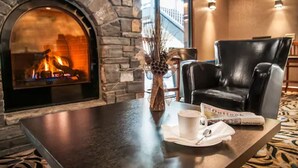 A stone fireplace with a fire, a leather chair, a table with a mug, and a vase with decorative branches. - Charltons Banff (Banff)