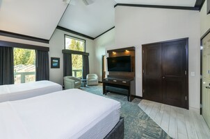 Habitación de hotel con dos camas, televisión, escritorio y un ventanal con vistas a árboles.