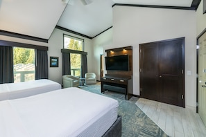 A hotel room with two beds, a TV, a desk, and a large window with a view of trees.