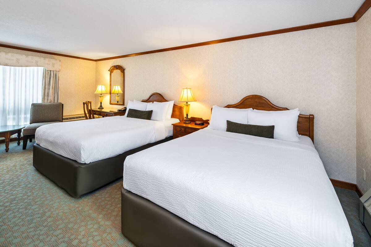 A hotel room with two beds, a desk, a chair, and a large window with curtains.