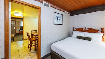 A hotel room with a bed, a dining table with chairs, a framed picture on the wall, and a wooden ceiling.