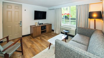 Uma sala de estar com sofá, mesa de centro de madeira, televisão e janela com cortinas.